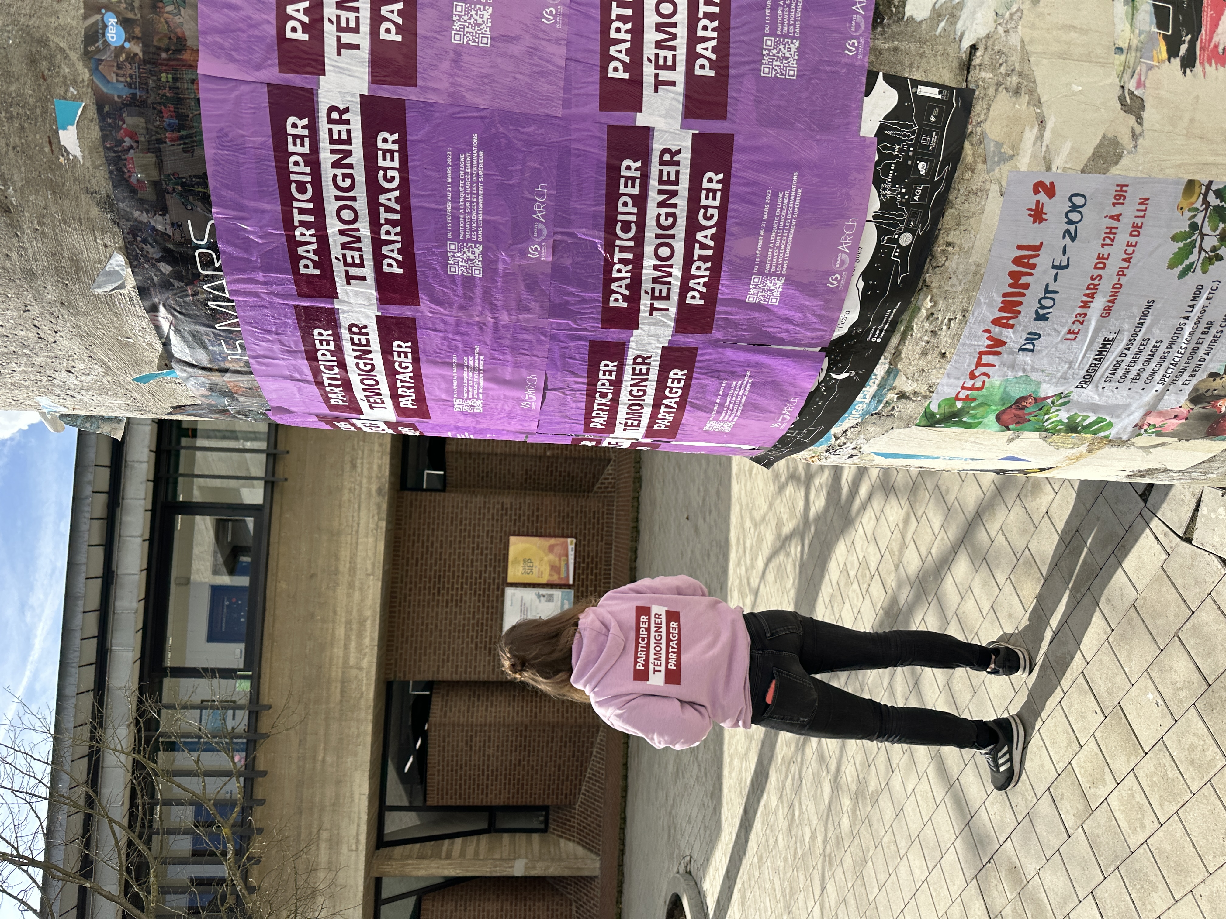 Ambassadrice devant un pilier de campus recouvert d'affiches BEHAVES