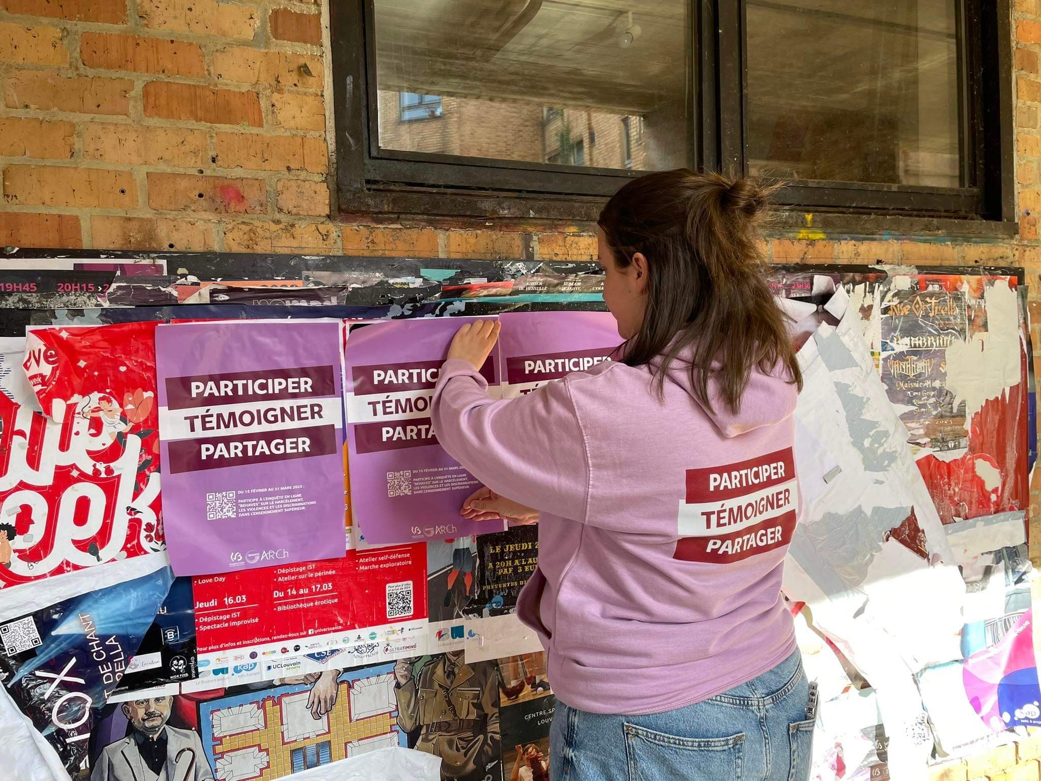 Ambassadrice posant des affiches BEHAVES sur un mur de brique