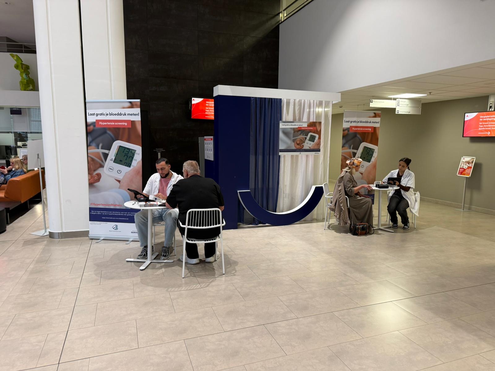 Deux tables de dépistage dans le hall d'un hôpital néerlandophone, ambassadeurs avec tablette